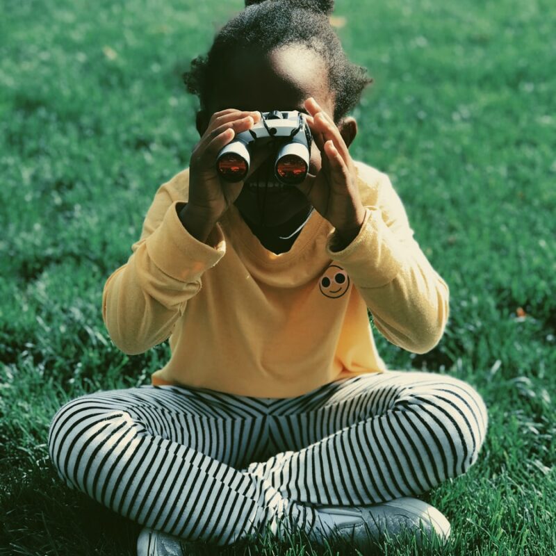 girl sitting on grass field holding binoculars